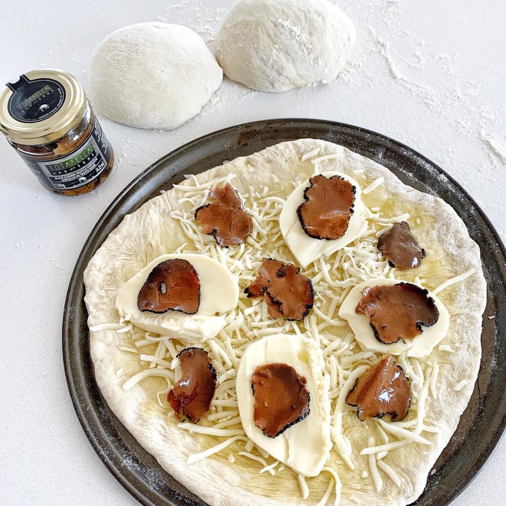 White pizza dough topped with mozzarella and black truffle carpaccio before baking