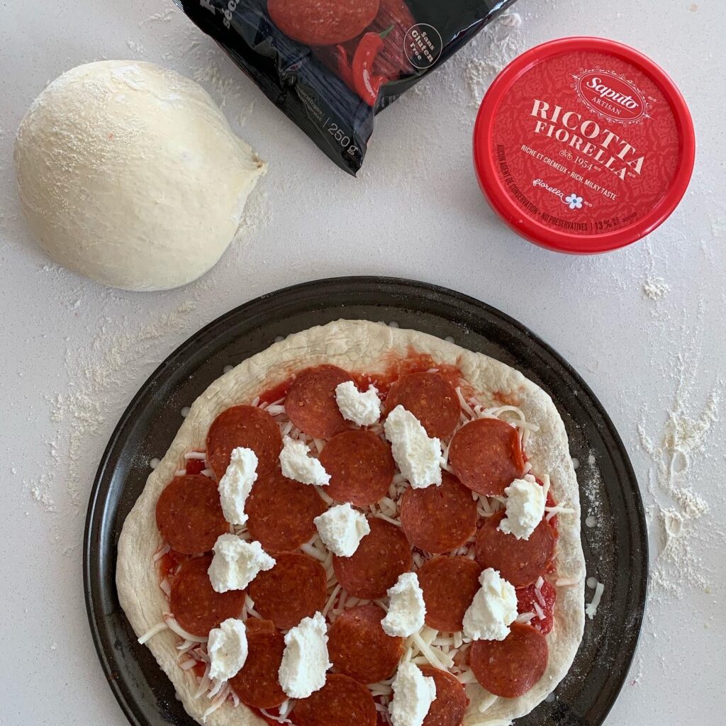 Assembling white pizza dough with pepperoni and ricotta before baking