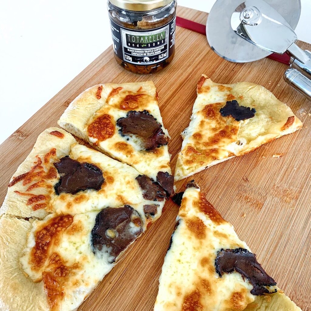 White pizza topped with black truffle carpaccio and melted cheese, sliced and ready to serve