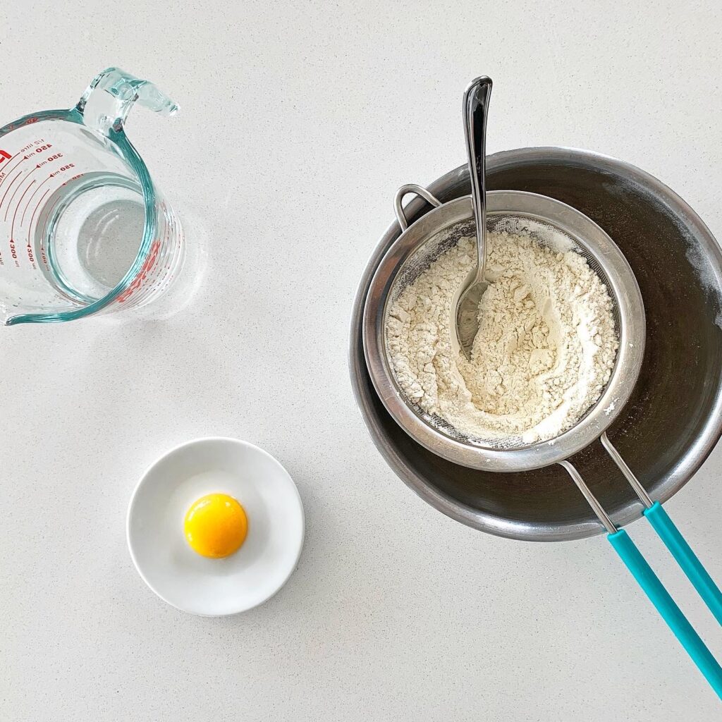 Ingredients for Coca de Recapte dough including flour, olive oil, and egg yolk prepared on a counter.