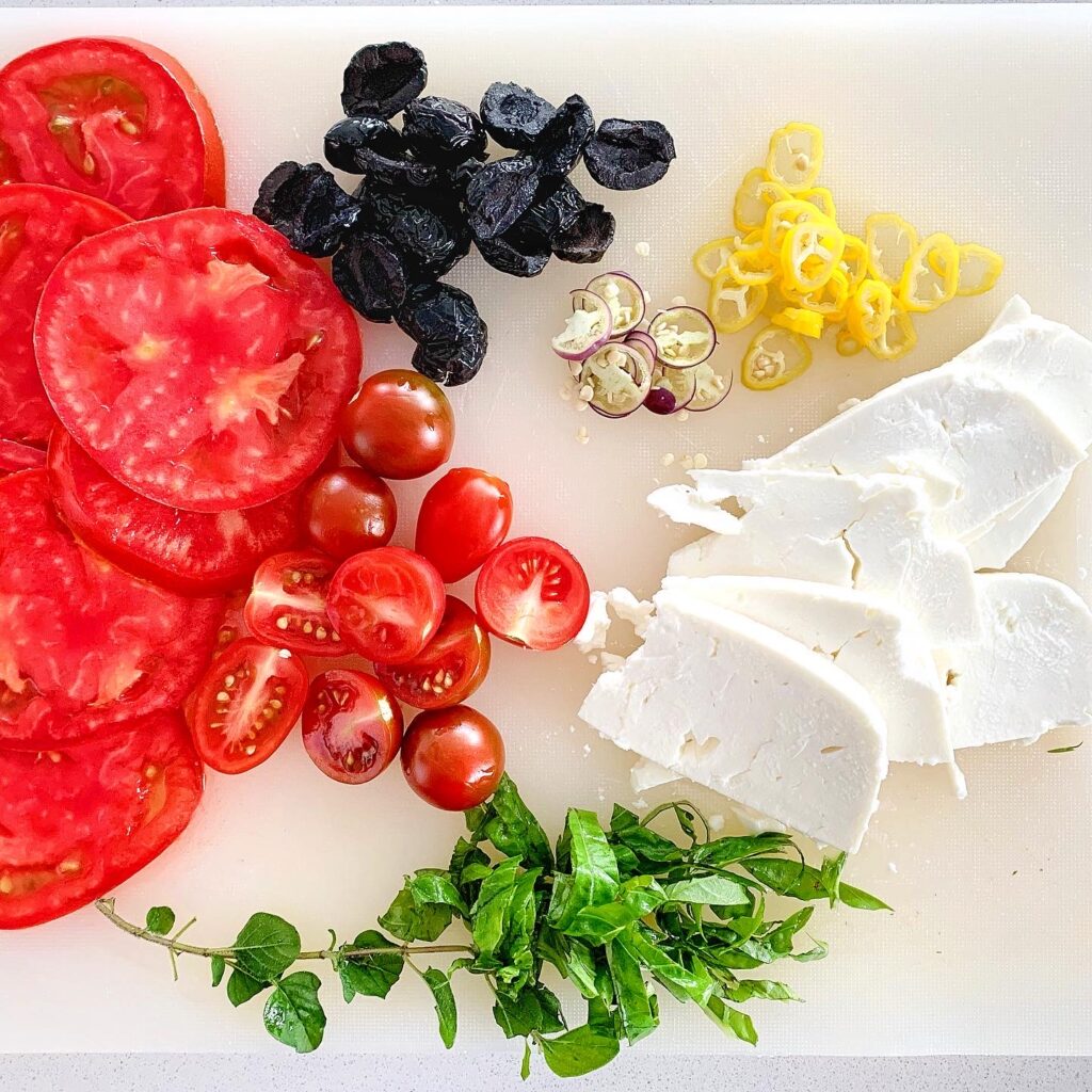 Fresh sliced tomatoes, red peppers, and olives prepared as toppings for Mediterranean flatbread.