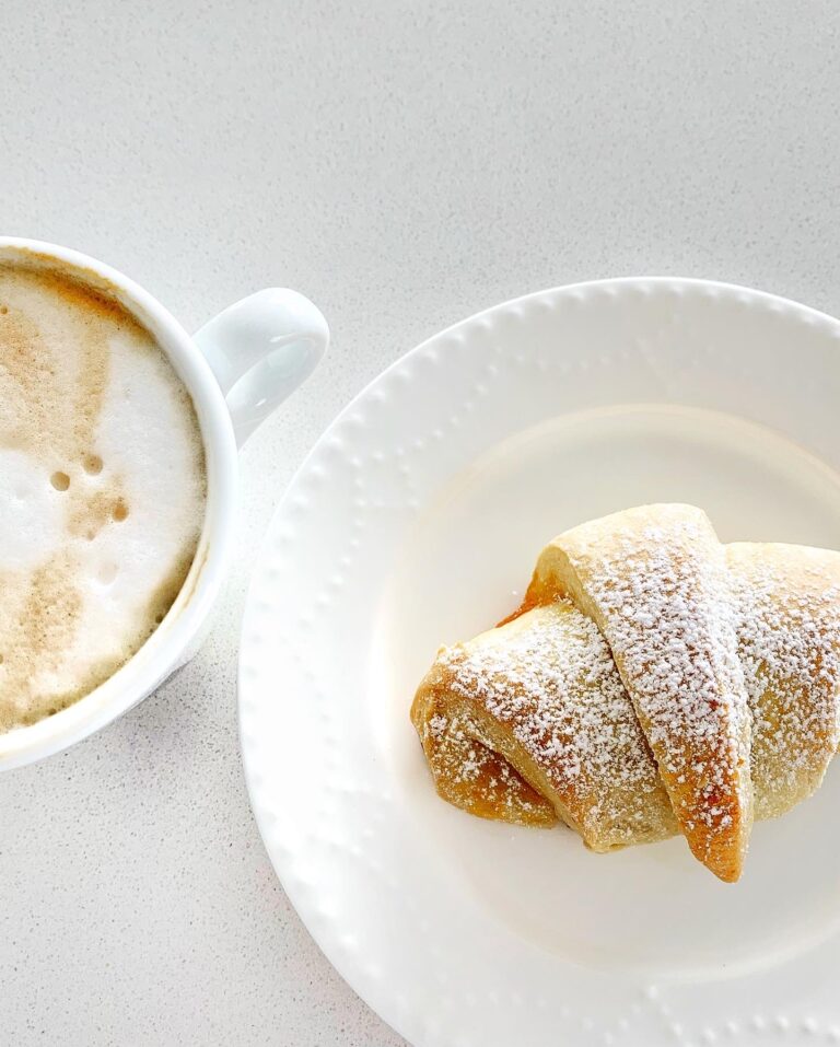 Homemade Italian cornetti served with cappuccino on a white plate, dusted with powdered sugar.