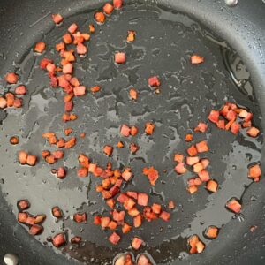 Crisping diced pancetta in a frying pan with rendered fat.