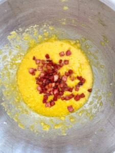 Whisked eggs and cheese with pancetta added in a mixing bowl for carbonara.