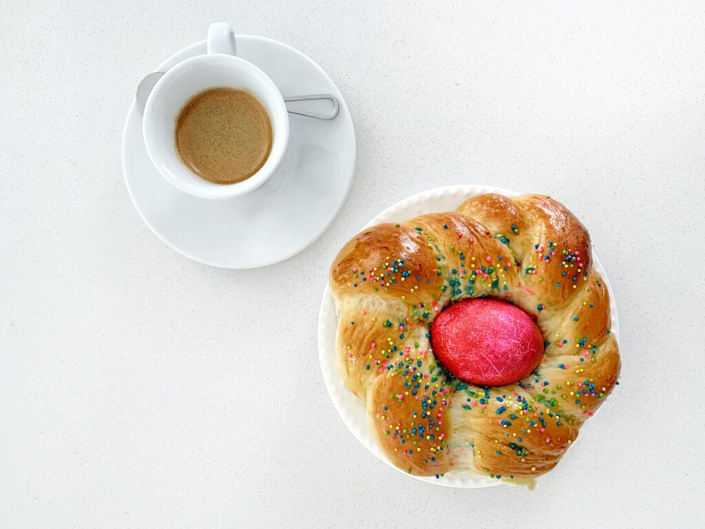 Traditional Italian Easter bread (pane di Pasqua) topped with sprinkles and a dyed egg, served with espresso