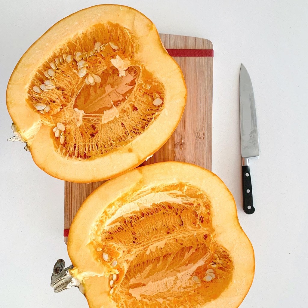 Fresh pumpkin cut in half on a cutting board, ready to be roasted for homemade pumpkin puree.