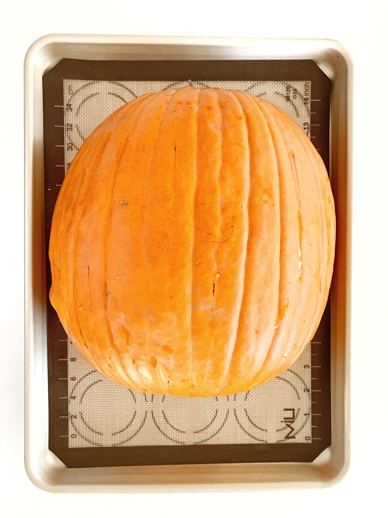 Whole pumpkin placed on a baking sheet to be roasted for pumpkin pie.