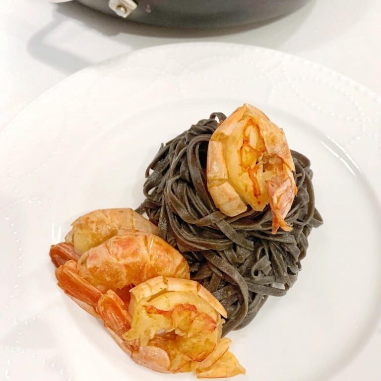 Plate of squid ink linguine with shrimp, fresh parsley, and garlic in a rich black pasta sauce.
