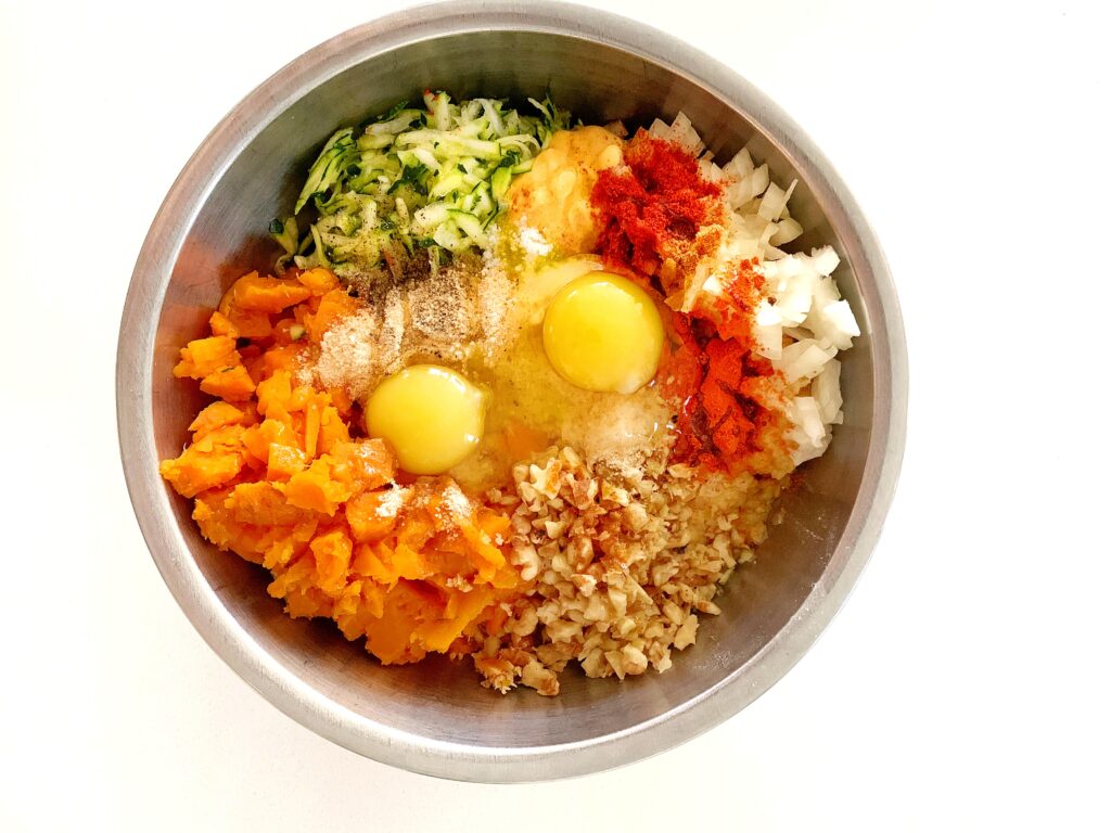 Veggie ball mixture with sweet potato, zucchini, onion, eggs, and seasoning in a mixing bowl