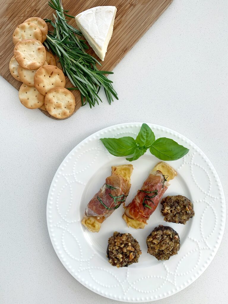 Wine tasting appetizers with baked prosciutto wrapped peaches, brie, and stuffed mushrooms on a serving plate