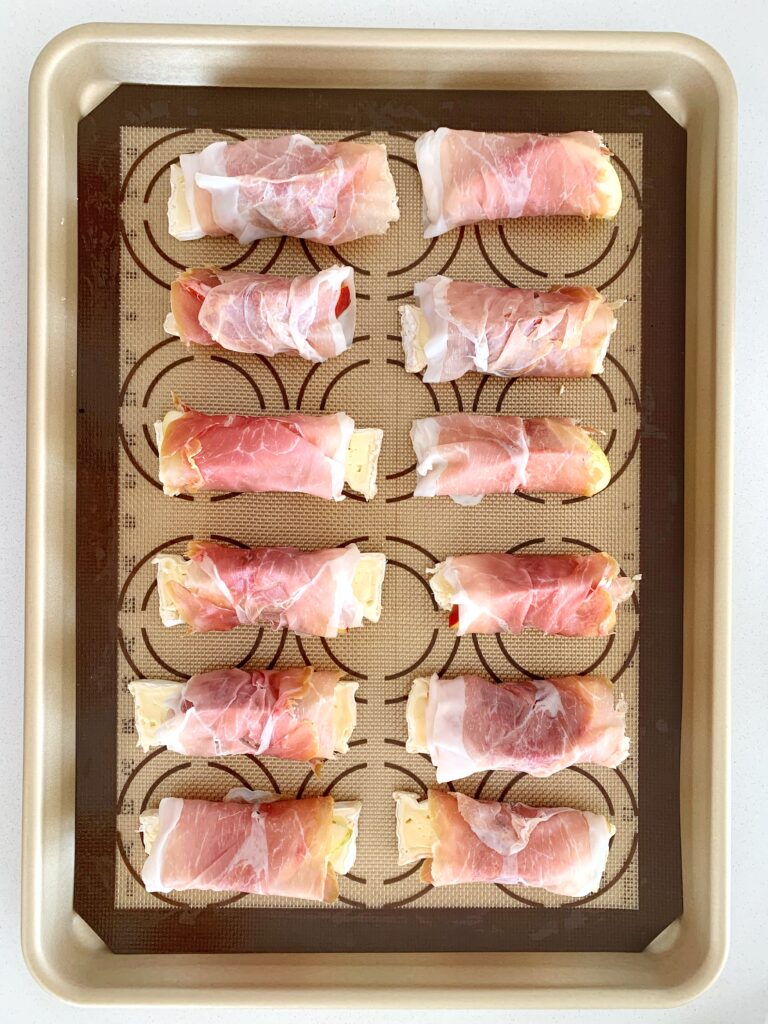 Unbaked prosciutto wrapped peaches and brie arranged on a baking sheet before roasting